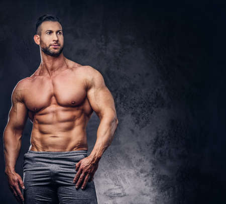 Portrait of a shirtless tall huge male with a muscular body with a stylish haircut and beard, in a sports shorts, posing in a studio.の写真素材