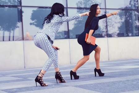 Two businesswomen dressed in stylish formal clothes, have fun in a downtown against a skyscraper.の写真素材