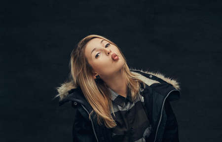 Portrait of a sexy blonde girl in a winter jacket and fleece shirt, standing in a studio.