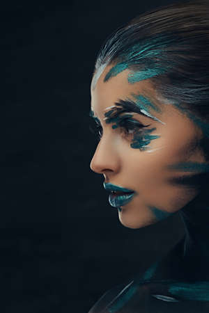 A young sensual girl with creative make-up. Blue and black shadows painted on her face. Conceptual idea.の写真素材