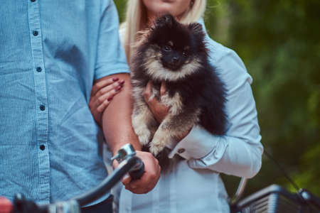 An attractive couple of a blonde female and man dressed in casual clothes on a bicycle ride with their cute little spitz in the park.の写真素材