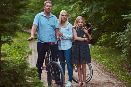 An attractive family dressed in casual clothes on a bicycle ride with their cute little spitz dog,...