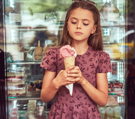 Beauty little girl in a fashionable dress eating strawberry, standing in an ice cream parlor.