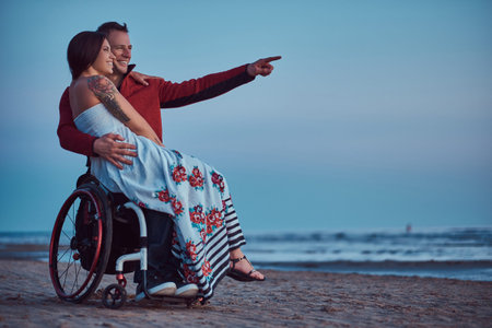 Loving couple, a woman sits on her husbands lap, resting on a beach against a background of a bright...