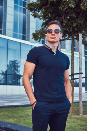 Young handsome fashionable man with a stylish haircut in sunglasses, dressed in a black t-shirt and...