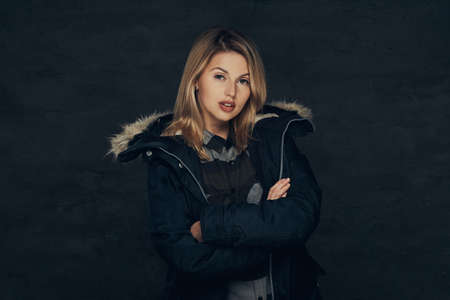 Portrait of a sexy blonde girl in a winter jacket and fleece shirt, standing in a studio.の写真素材