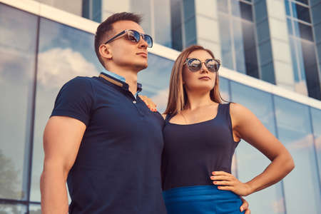Attractive fashionable couple, sexy blonde girl and handsome man standing in the modern city against a skyscraper.の写真素材