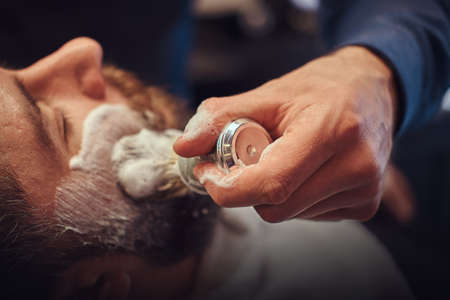 Master hairdresser prepares the face for shaving and smears the face with foam in a hairdressing salon.の写真素材