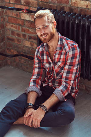 Young handsome redhead model man sits on a floor in the room with a loft interior.の写真素材