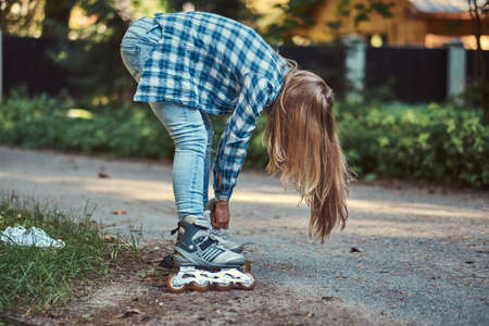Beautiful girl with long hair wearing fleece shirt and jeans putting on rollers in the park in...