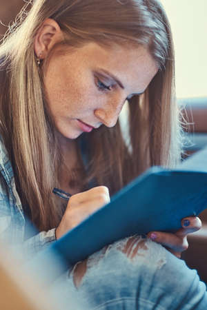 Portrait of a charming girl making notes in a notepad, sitting in a car.