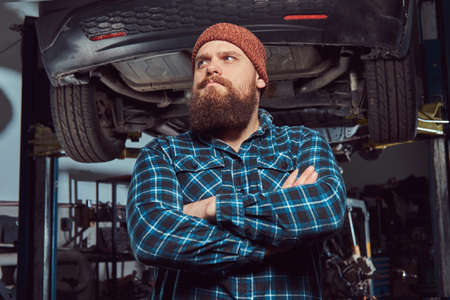 Two bearded brutal mechanics repair a car on a lift in the garage.の写真素材