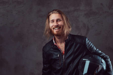 Portrait of a handsome stylish redhead biker in a black leather jacket, holds motorcycle helmet, posing in a studio.の写真素材