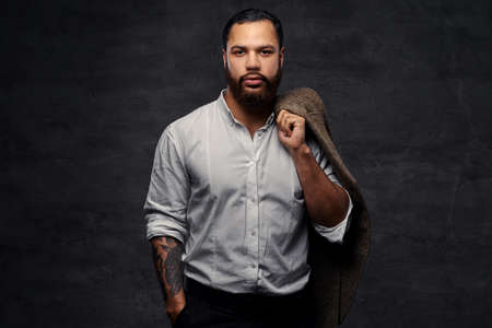 Handsome African-American man with a tattoo on his arm, dressed a white shirt, holds a jacket on a...
