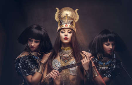 Portrait of haughty Egyptian queen in an ancient pharaoh costume with two concubines.の写真素材