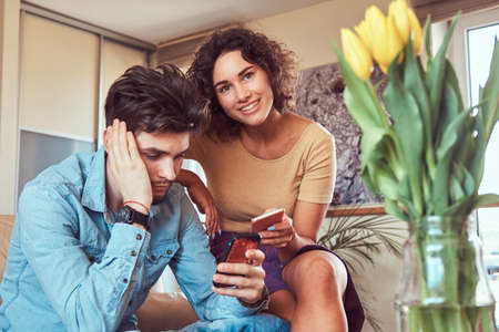 Hispanic couple relaxing together on the sofa. Using smartphones while resting at home.