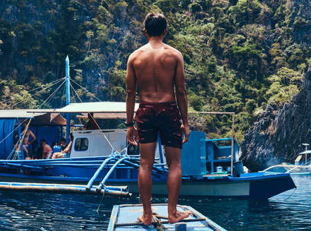 Shirtless Asian guy standing on a bow of the ship on the background of a beautiful landscape of...