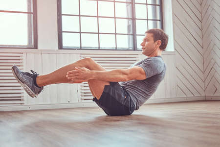 Handsome fitness man in a t-shirt and shorts doing abdominal exercises on floor at home.の写真素材