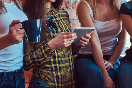 Group of female friends in casual clothes discussing while looking something on a digital tablet in a room with loft interior.の写真素材