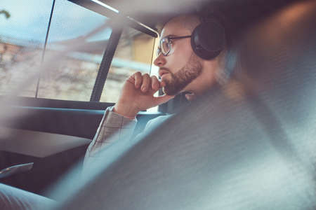 Successful stylish young businessman in a gray suit and pink shirt, riding on a back seat in a luxury car.の写真素材