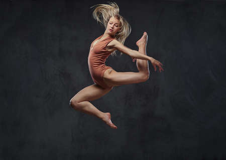 Young graceful ballerina dances and jumps in a studio. Isolated on a dark background.の写真素材