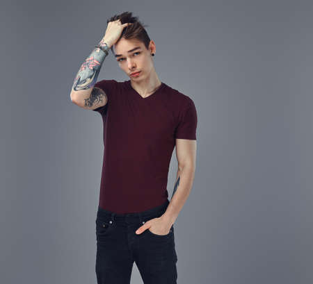 Handsome fashionable young guy with stylish hair and tattoo on his arm posing in a studio.