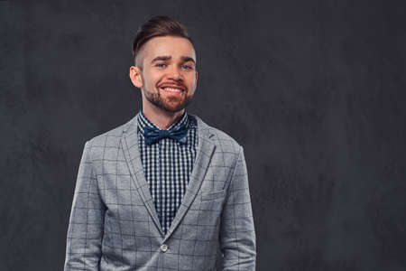 Smiling stylish bearded man with hairstyle in an elegant retro gray suit and bow tie, posing in a studio.の写真素材