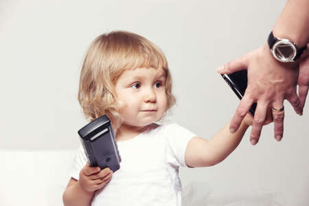 Portrait of a cute little girl in a white dress holds a tv remote on white background.