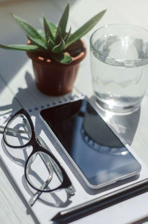 Top view of smartphone, notebook with pencil, glass of water and pots with flowers at workplace.の写真素材