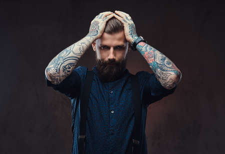 Desperate old-fashioned hipster guy in a blue shirt and suspenders standing in a studio.の写真素材