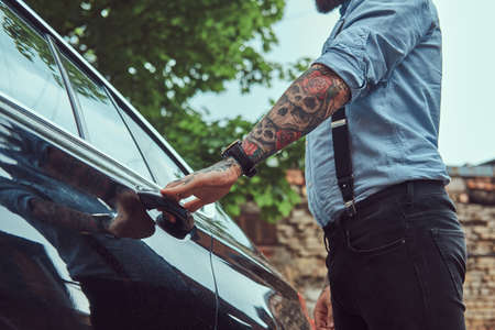 Cropped image of an old-fashioned tattooed man in a shirt with suspenders, who is going to get into a car.の写真素材