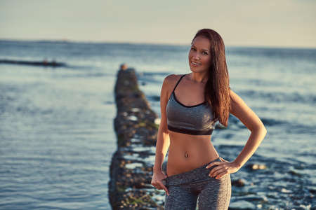 Beautiful fitness woman in a gray sportswear posing against a sea background.の写真素材