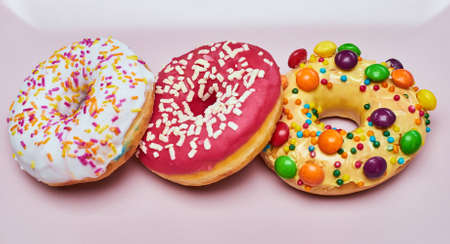 Three appetizing donuts lie on a pink ceramic plate.