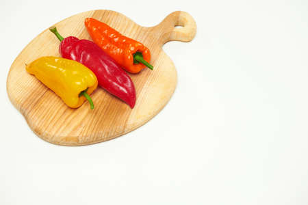 Several different colored bell peppers lie on a wooden cutting board.の写真素材