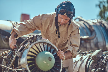 Portrait of a mechanic in uniform and flying helmet, repairing the dismantled airplane turbine.