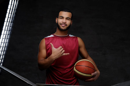 Young African-American basketball player in sportswear isolated over dark background.
