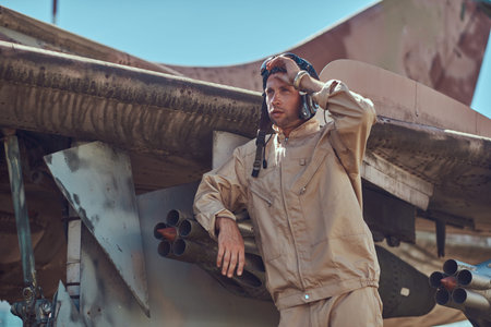 Pilot in uniform and flying helmet standing near an old war fighter-interceptor.