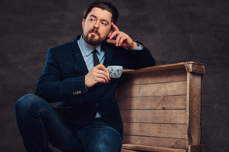 Pensive middle age businessman with stylish hair and beard dressed in jeans, jacket and tie, sitting...