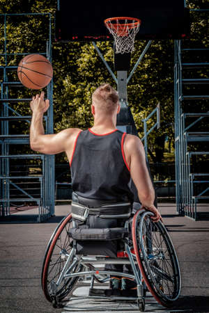 Back view of a disabled basketball player in wheelchair spinning basketball on his finger on open gaming ground.の写真素材