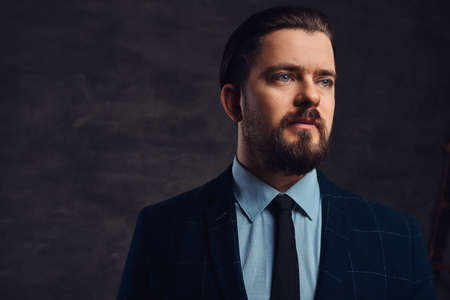 Close-up portrait of a handsome middle-aged man with beard and hairstyle dressed in an elegant formal suit. Isolated on a textured dark background in studio.の写真素材