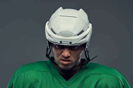 Close-up portrait of an angry professional hockey player in a protective sportswear and helmet on a gray background.の写真素材