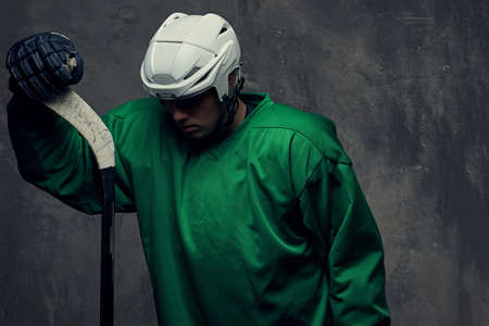 Hockey player wearing green protective gear and white helmet standing with the hockey stick. Isolated on a gray background.の写真素材