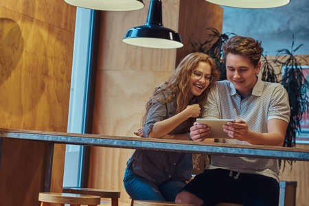 Happy couple students using a digital tablet while sitting at a table in the college canteen during a break.の写真素材