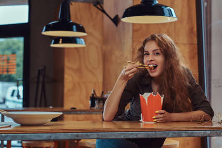 Young redhead female eating spicy noodles in an Asian restaurant.の写真素材