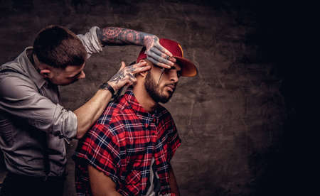 Handsome bearded African American guy in a fleece shirt and cap getting a haircut by an old-fashioned professional hairdresser does haircut.の写真素材