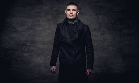 Tattoed young guy in a black jacket posing at the studio. Isolated on dark textured background.の写真素材