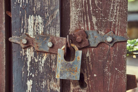 Close-up image of a vintage rusted lock on an old worn wooden fence.の写真素材