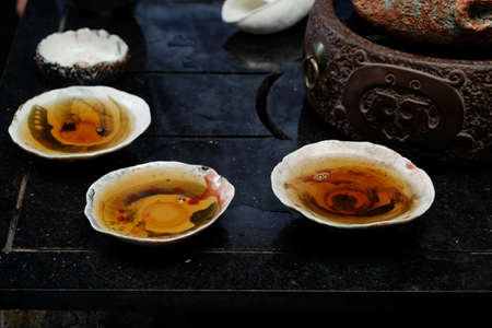 Tea ceremony concept. Close-up image of little ceramic saucers with brown tea on black wooden table.の写真素材