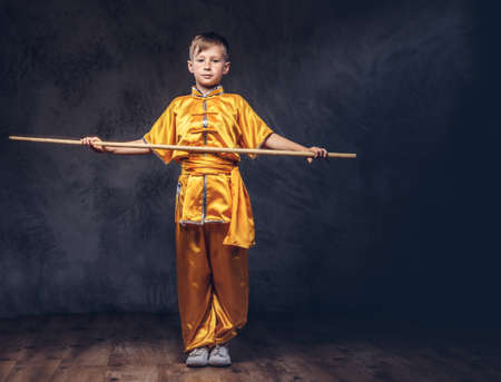 Cute boy dressed in the traditional costume of a Tibetan monk shows the tricks with dao stick from the wellness complex at a studio.の写真素材