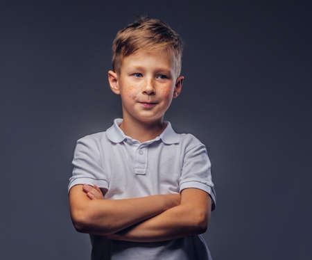 Cute little boy dressed in a white t-shirt standing with crossed arms in a studio. Isolated on gray background.の写真素材
